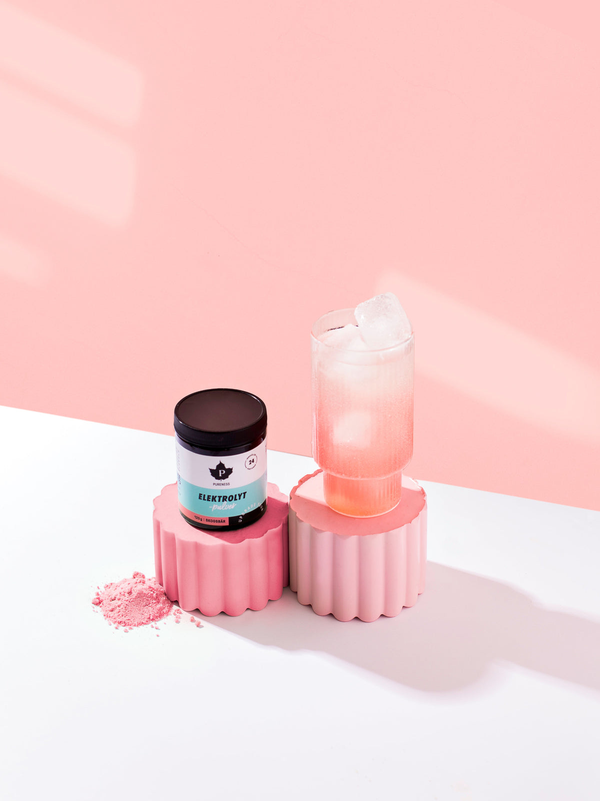 en burk elektrolyter med skogsbärsmak som står bredvid ett glas med blandad elektroytdryck, med en rosa vägg bakom dem.
