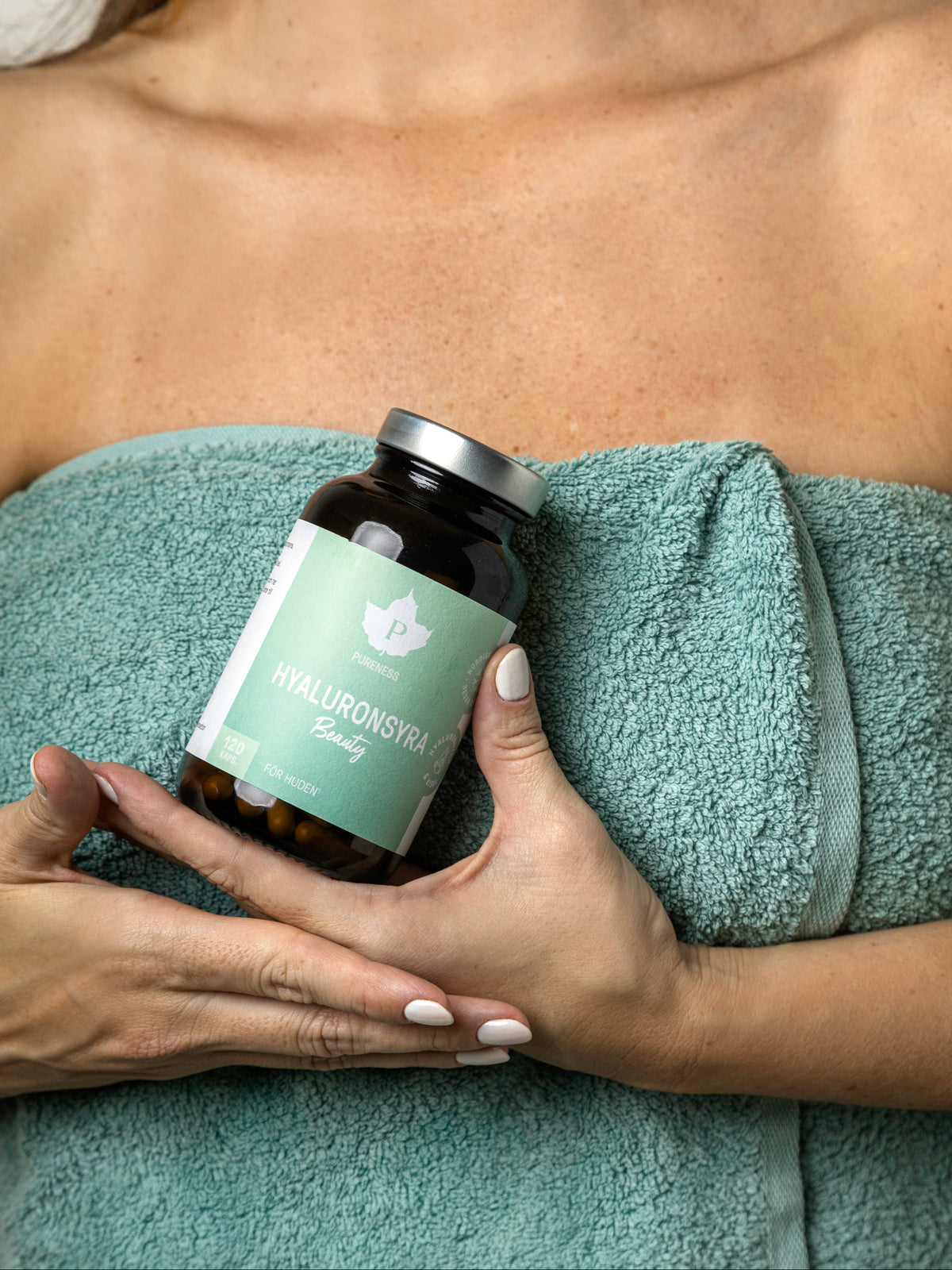 En kvinna med en handduk runt sig som håller i en burk hyaluronsyra