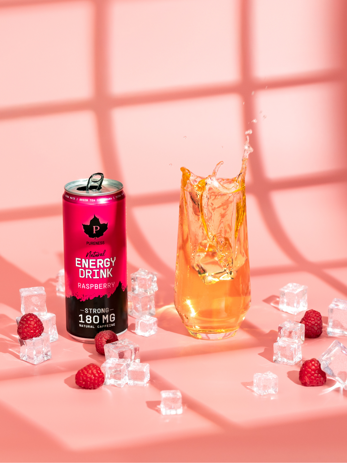 en burk natural energy drink hallon bredvid ett glas med drickan i sig och iskuber och hallon utspridda runt