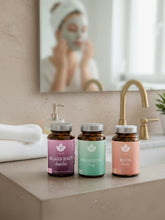 Ett badrum med kollagen beauty, hyaluronsyra beauty och biotin beauty på handfatets kant. I bakgrunden ser man en kvinna i spegeln som applicerar hudvård 