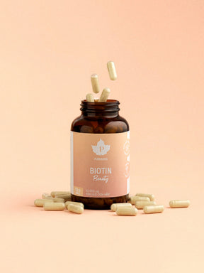 En burk biotin beauty med kapslar som flyger ut och en orange-rosa bakgrund