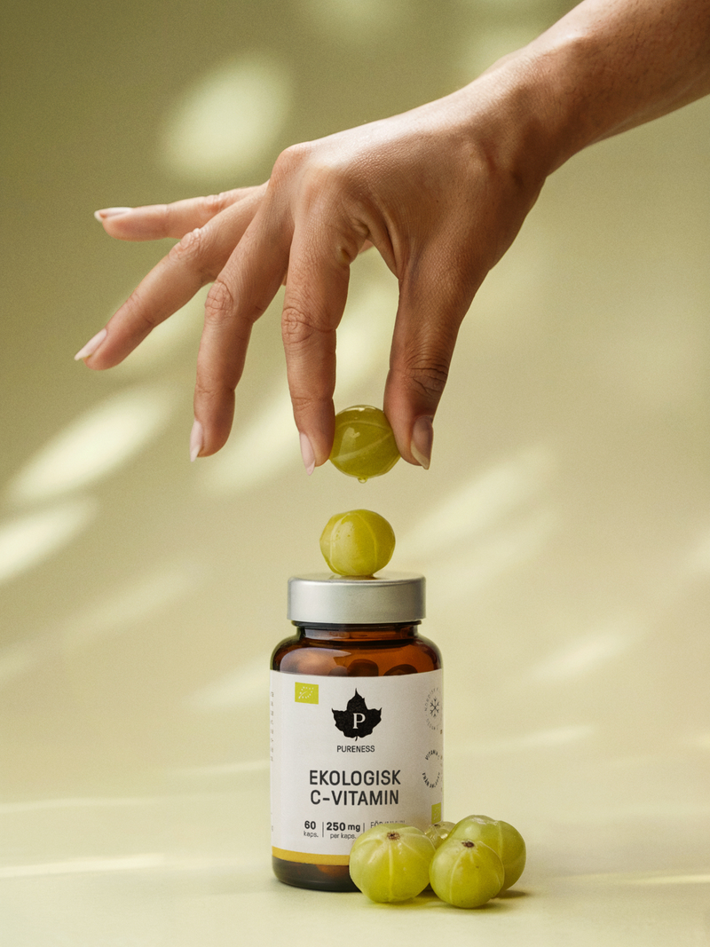 en hand som placerar ett grönt bär på en burk ekologisk c-vitamin med ljusgrön bakgrund