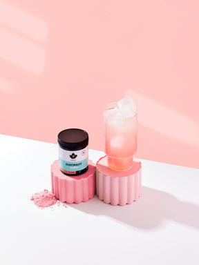 en burk elektrolyter med skogsbärsmak som står bredvid ett glas med blandad elektroytdryck, med en rosa vägg bakom dem.