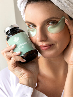 En kvinna med ögonmasker håller upp en burk hyaluronsyra kosttillskott bredvid sitt ansikte