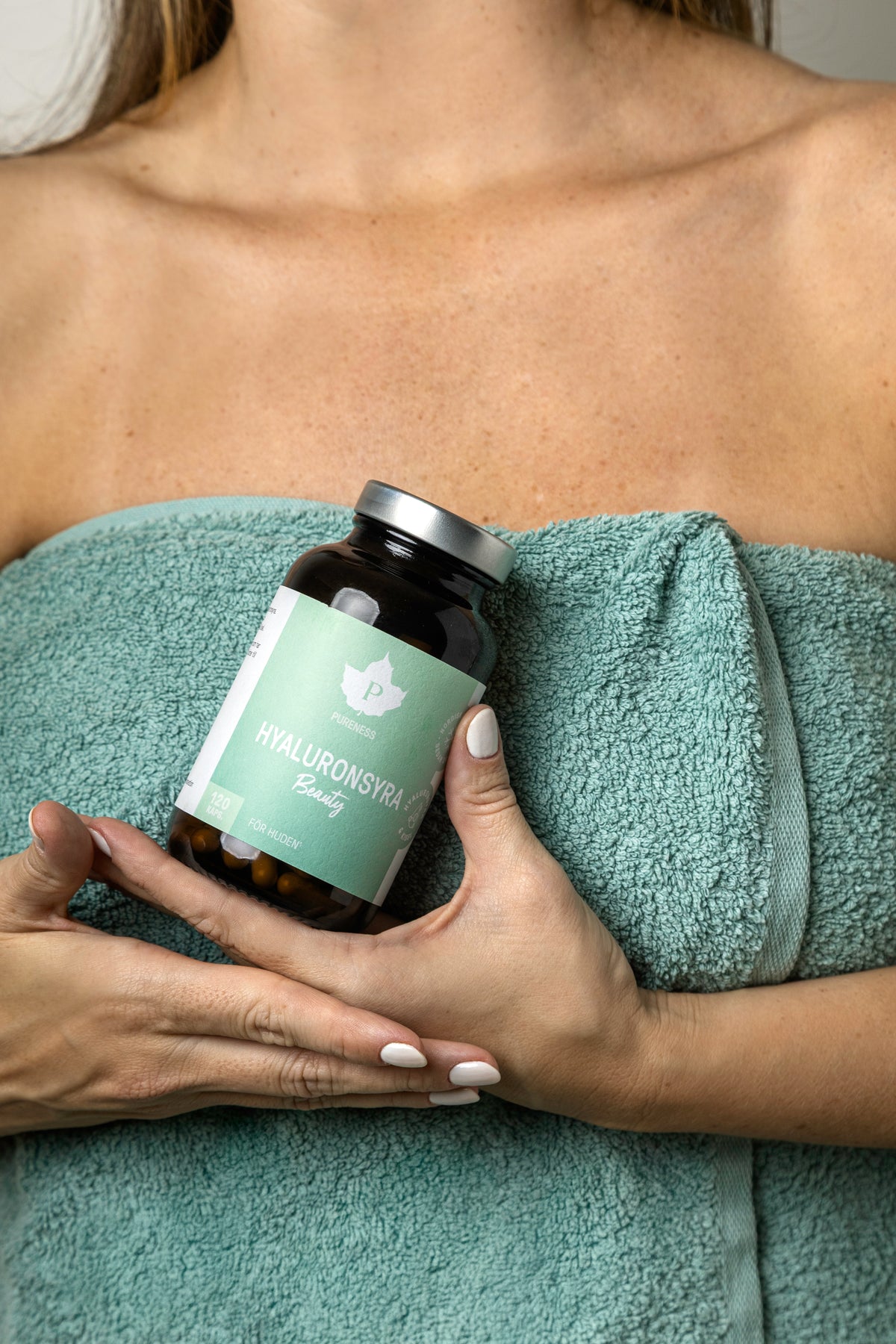 En kvinna med en handduk runt sig som håller i en burk hyaluronsyra