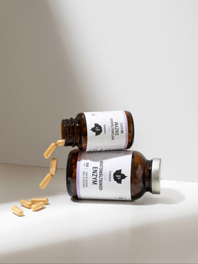 två burkar matsmältningsenzymer som ligger bredsides på varandra varav den övre är öppnad och spiller ut kapslar. Vit bakgrund.