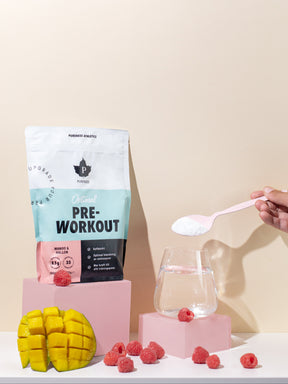 en påse preworkout som stor bredvid ett glas vatten där en hand häller i pre workout
