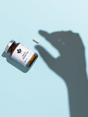 En ljusblå bakgrund med en liggandes burk trippel magnesium, med skugga av en hand bredvid som låtsas ta en kapsel.