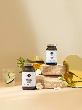 två burkar trippel zink, en står på 2 dekorationsstenar. bakgrunden har 2 små speglar, blommor och bredvid står ett glas med gurkvatten