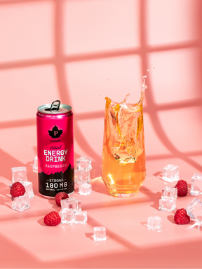 en burk natural energy drink hallon bredvid ett glas med drickan i sig och iskuber och hallon utspridda runt