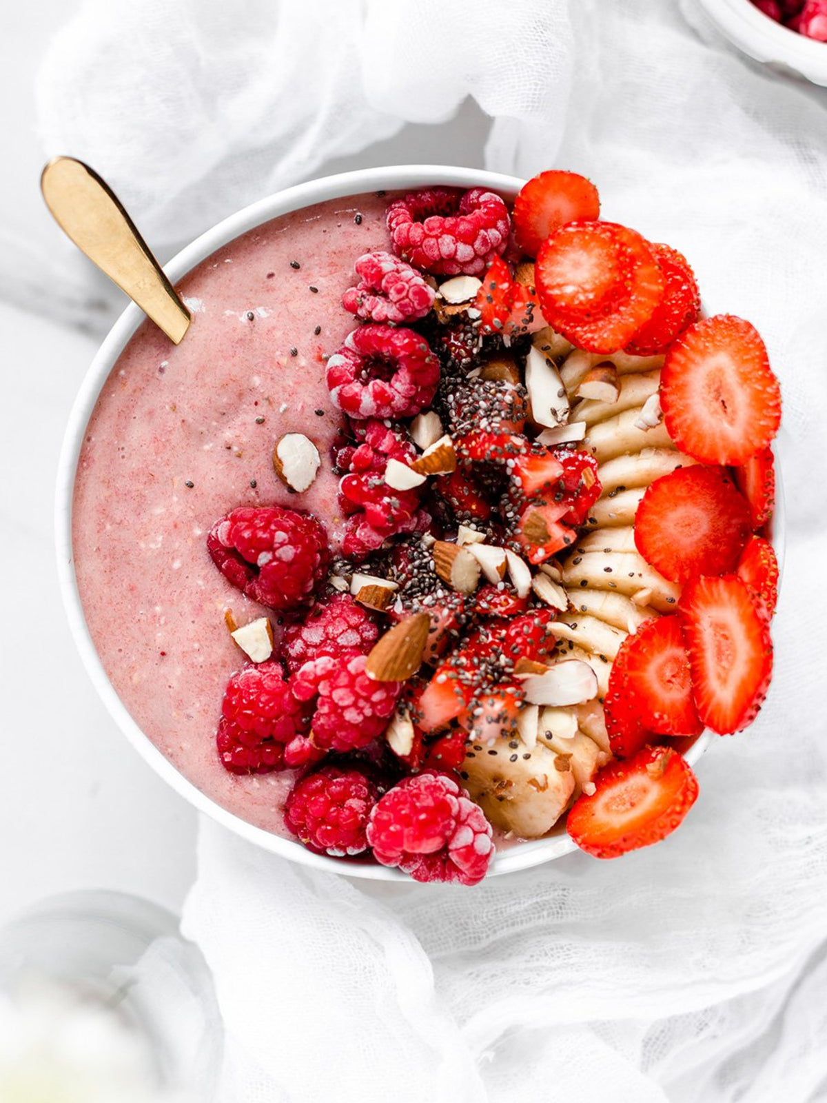 En smoothie bowl med hallon banan och jordgubb på ett bord med vit dekor