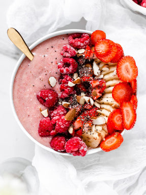 En smoothie bowl med hallon banan och jordgubb på ett bord med vit dekor